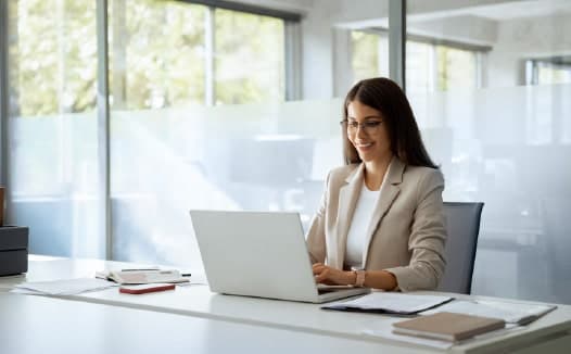 Businesswoman working on a laptop in a bright, modern office environment while reviewing B2B targeting or customer insights.
