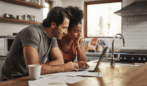 Couple reviewing home service paperwork together at a kitchen counter while using a laptop, representing the decision-making moments digital campaigns aim to influence.