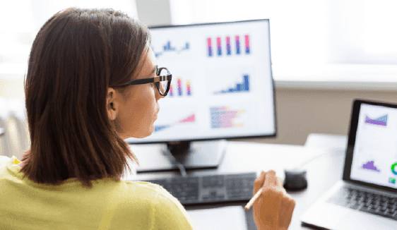 Healthcare marketer analyzing charts on dual monitors, reflecting data-driven optimization that improves patient engagement and appointment growth.