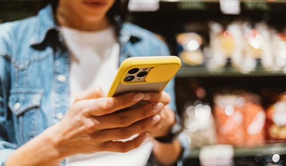 Person checking their smartphone in a store, demonstrating mobile ads activated through addressable geo fencing.