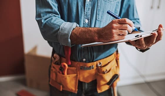 Contractor in a tool belt taking notes on a clipboard inside a home, representing household settings where home services decisions are made.