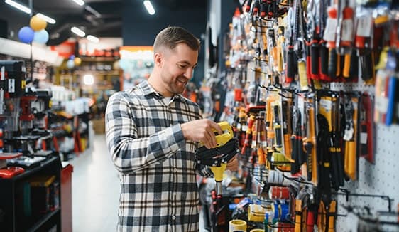 Man comparing power tools in a hardware store aisle, reflecting real-world local shopping behavior that home service brands can reach with digital campaigns.