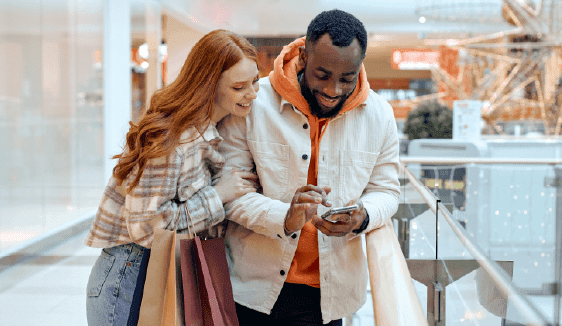 Shoppers checking a phone inside a mall, showing how online engagement supports multi-location business marketing.