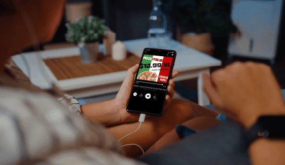 Person holding a smartphone displaying an in-app audio companion banner ad, illustrating how programmatic audio ads can include clickable extensions for deeper engagement.