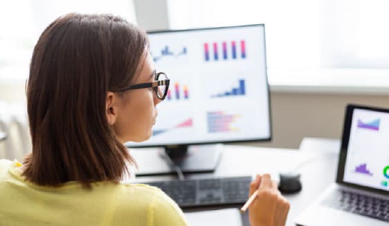 Marketer reviewing video performance metrics on multiple screens, highlighting transparent reporting and real-time insights.