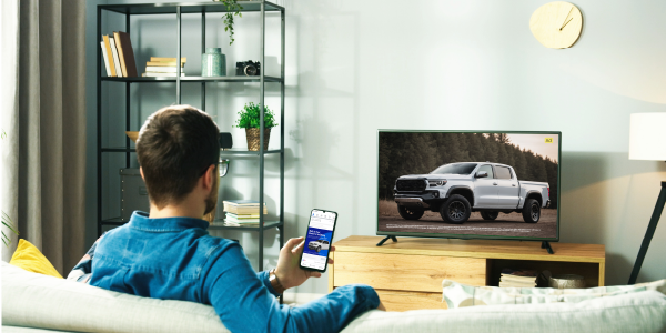 Person sitting on a couch scrolling their phone while a streaming TV automotive advertisement for a pickup truck plays on a large screen in a modern living room.